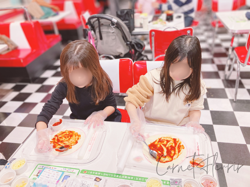 ピザ作り体験中の子どもたちが、トマトソースを生地に広げている様子|カンドゥーの食事スペースにて