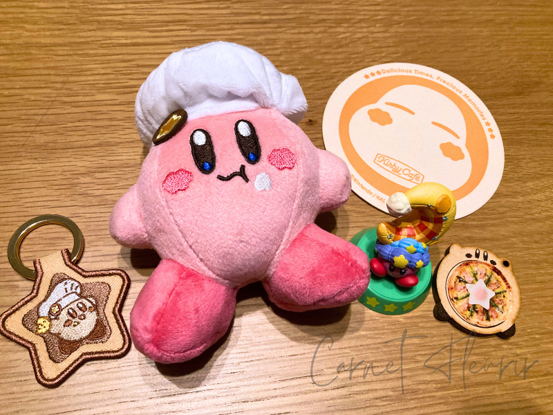 購入したグッズの画像。刺繍キーホルダー、カービィマスコット、ディープスリープマスコット、ピザ型マグネット、ランダムコースター