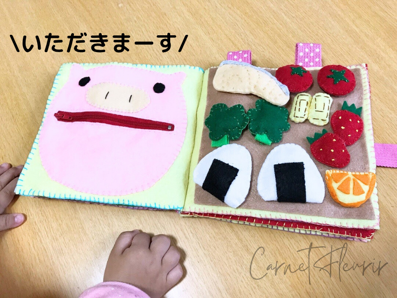 フェルト製のやわらかなパーツでお弁当が作られている。左ページは豚の口にチャックがついていて、パーツを収納できるようになっている。