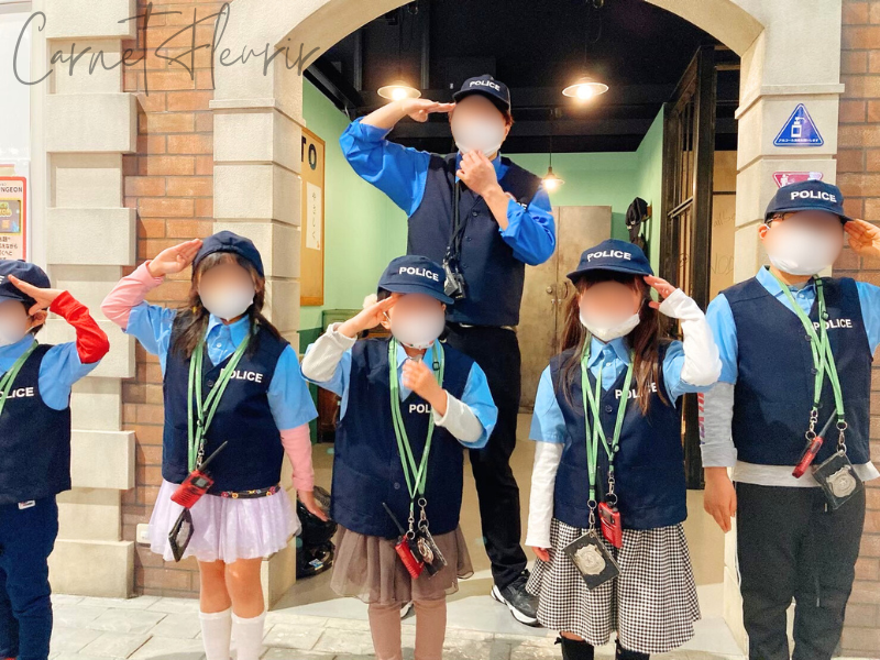 警察官の制服を着て敬礼ポーズをとる子どもたち|カンドゥーの警察体験ブース前にて