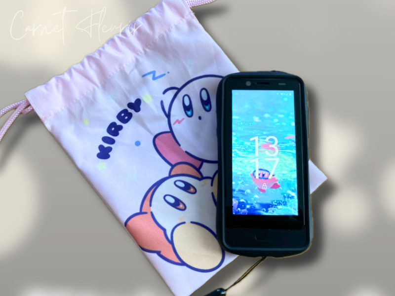 カービィの巾着袋と並べたHamic端末。現在の待ち受け画面は水色の海モチーフ
