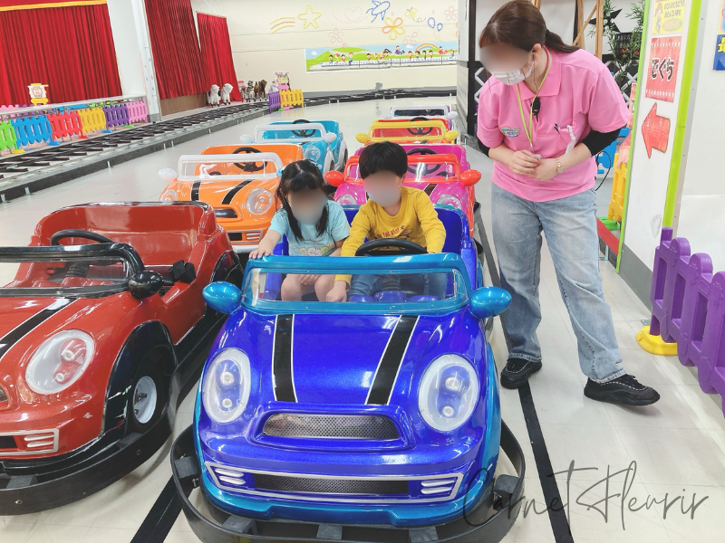 ゴーカートに乗って楽しむ子どもたち。青い車に2人で乗り、スタッフがそばで見守っている様子。