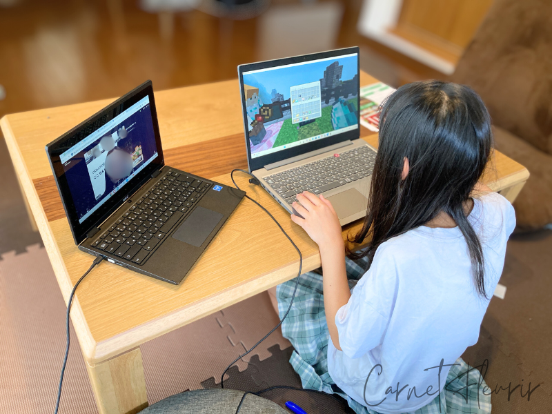 マインクラフトの画面を操作する小学生の女の子。ノートパソコンでプログラミング体験中