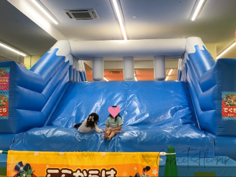 巨大な青いふわふわすべり台の前でくつろぐ子どもたち