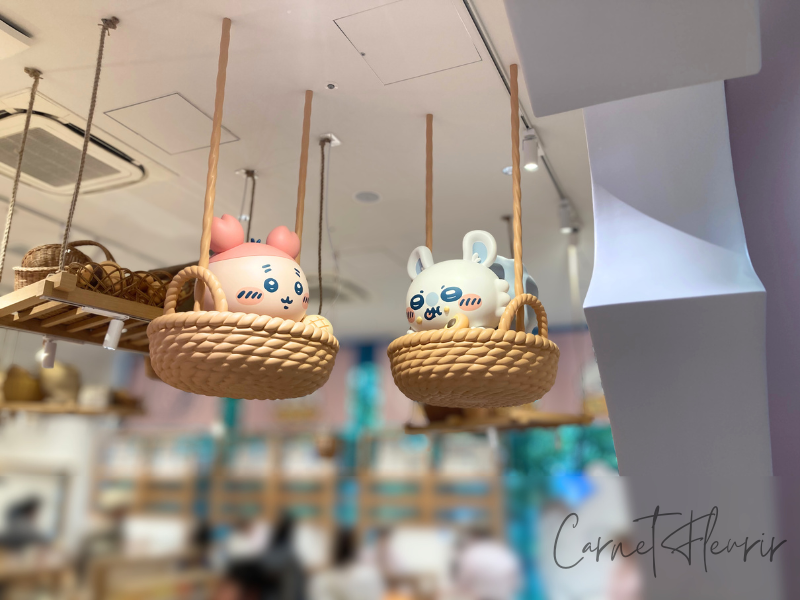 ちいかわベーカリー店内の天井に飾られた、バスケットに入ったモモンガとカニちゃんの立体フィギュア