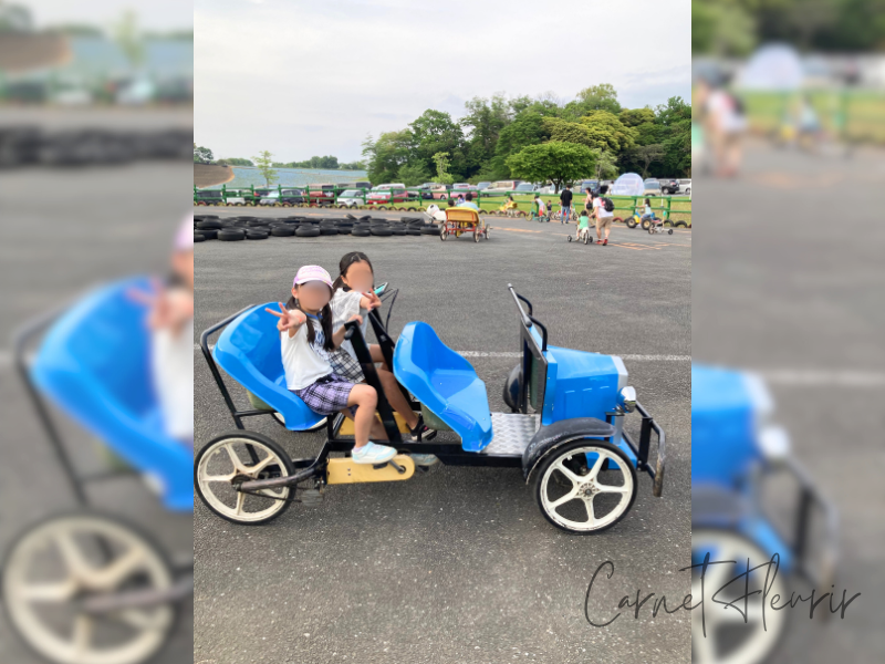 東京ドイツ村のパークエリアで楽しむおもしろ自転車。青いユニークな車型の自転車に乗ってポーズをとる子どもたち