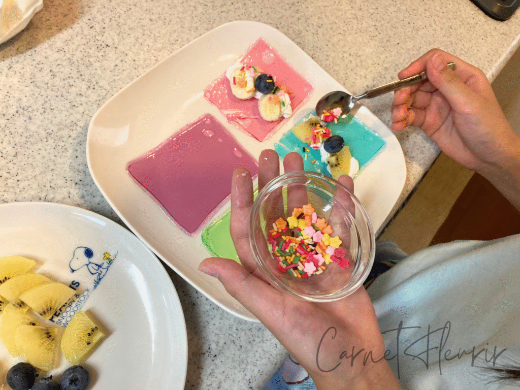 ゼリークレープにホイップやフルーツをのせ、トッピングを飾る子どもの手元