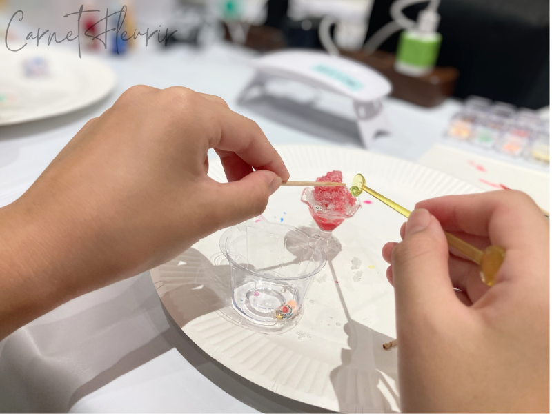 フルーツパーツをレジンにくぐらせ、かき氷にのせている様子