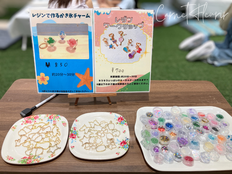 横浜ノースポートモールのレジンワークショップで使われるチャーム土台とデコ素材の展示。かき氷チャームやマーメイドキーホルダーの案内看板あり