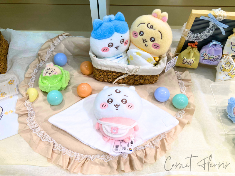 おくるみに包まれたちいかわたちがバスケットや布の上に並べられた展示。キャベツにくるまれたうさぎや、カラーボールも添えられている。
