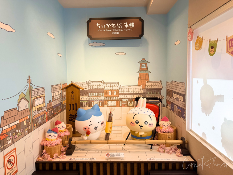 ハチワレ。うさぎのフォトスポット。川越の街並みを背景に、ハチワレは両手にお菓子をもっている。うさぎは車夫の恰好をしている。